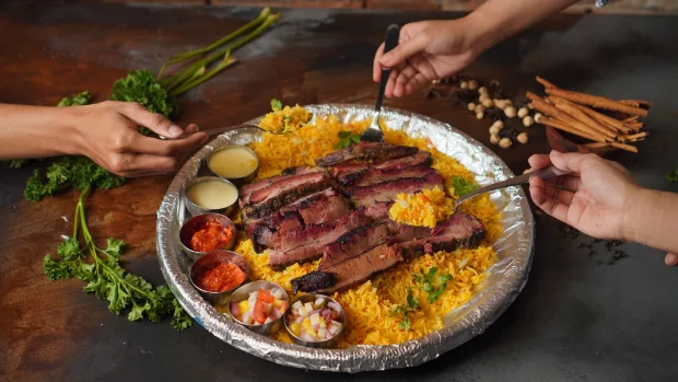 Grilled meat platter being served with both hands